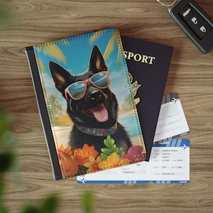 Op de afbeelding: Een zwarte paspoorthouder met een cartoonhond met zonnebril op een strand. Daarnaast een marineblauwe paspoort, vliegtickets en een autosleutel. De tickets tonen vluchtinformatie. Het product is van leer.