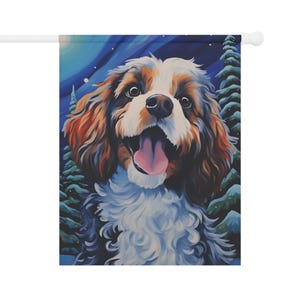 May include: A decorative garden flag featuring a happy Cavalier King Charles Spaniel dog with a pink tongue, set against a wintery blue and green background with snow-covered trees. The dog has brown, white, and black fur.