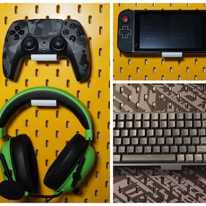 Puede incluir: Un tablero de clavijas amarillo con un auricular para juegos verde, un mando de videojuegos de camuflaje negro y gris, una consola de videojuegos portátil negra y un teclado negro y gris.