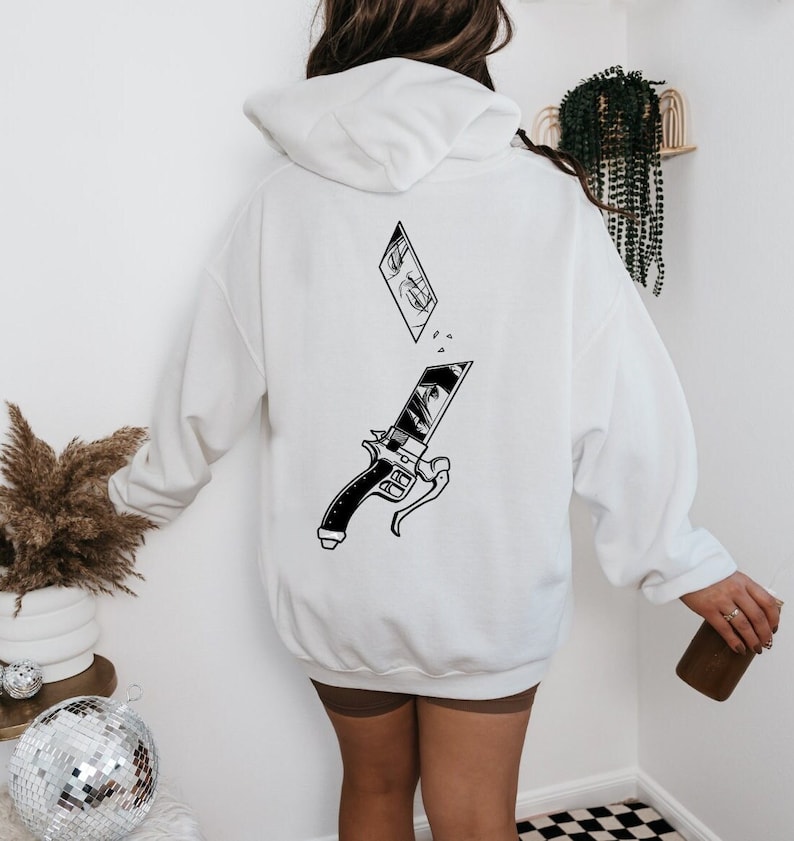 May include: White hooded sweatshirt with a black and white graphic print of a sword and a broken piece of a comic book panel with an eye. The graphic is on the back of the sweatshirt.