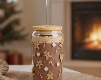 Könnte beinhalten: Ein klares Glas mit heißer Schokolade, verziert mit Lebkuchenmännern, Zuckerstangen und Marshmallows. Es hat einen Bambusdeckel und einen durchsichtigen Glasstrohhalm. Im Hintergrund ein Weihnachtsbaum und ein Kamin.