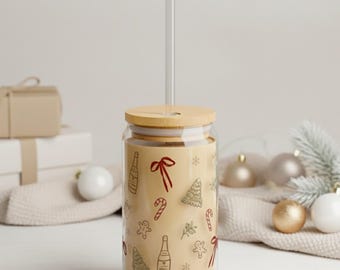 Könnte beinhalten: Ein klares Glas mit einem Bambusdeckel und einem durchsichtigen Strohhalm. Der Becher ist mit festlichen roten und braunen Illustrationen zum Thema Feiertage verziert, darunter Schleifen, Bäume und Zuckerstangen. Der Becher ist mit einer hellen Flüssigkeit gefüllt.