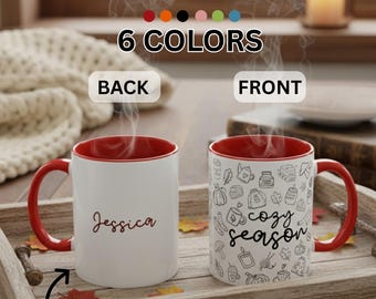 Könnte beinhalten: Weiße Keramik-Tasse mit rotem Innenraum und Henkel. Die Vorderseite der Tasse hat ein schwarz-weißes "cozy season"-Design. Auf der Rückseite der Tasse steht der Name "Jessica" in Schreibschrift. Der Text "YOUR NAME HERE" ist ebenfalls sichtbar.