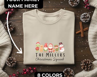 Könnte beinhalten: Beiges Rundhals-T-Shirt mit einem Weihnachtstrupp-Motiv. Das Motiv zeigt Zeichentrickfiguren, darunter den Weihnachtsmann, einen Schneemann und Elfen. Der Text auf dem Shirt lautet "The Millers Christmas Squad". Das Shirt hat auch den Text "Your Family Name Here" und "8 Colors".