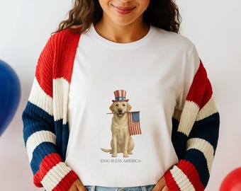 Könnte beinhalten: Weißes T-Shirt mit einem Labrador Retriever, der einen patriotischen Zylinder trägt und eine amerikanische Flagge hält. Der Text "-DOG BLESS AMERICA-" ist darunter gedruckt. Die Person trägt eine rot-weiß-blau gestreifte Strickjacke.