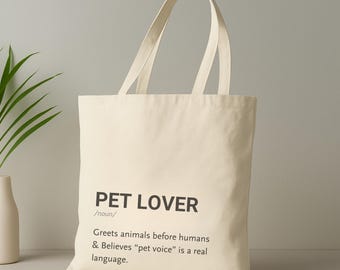 Könnte beinhalten: Cremefarbene Tragetasche mit schwarzem Text: "PET LOVER /Substantiv/ Begrüßt Tiere vor Menschen & Glaubt, dass "Tierstimme" eine echte Sprache ist." Die Tasche hat zwei lange Griffe und ist aus robustem Stoff.