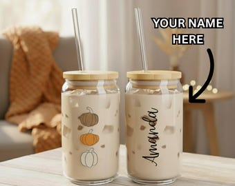 Könnte beinhalten: Zwei transparente Glasbecher mit Bambusdeckeln und durchsichtigen Strohhalmen. Einer hat Kürbis-Illustrationen, der andere den Namen "Amanda". Der Text "YOUR NAME HERE" befindet sich über dem zweiten Becher.