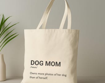 Könnte beinhalten: Cremefarbene Canvas-Tragetasche mit schwarzem Text: "DOG MOM /Substantiv/ Besitzt mehr Fotos von ihrem Hund als von sich selbst." Die Tasche hat zwei lange Henkel.
