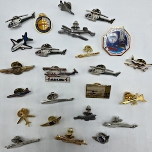 May include: A selection of aviation-themed lapel pins, featuring aircraft, helicopters, and a hot air balloon. The pins are made of metal and come in various colours and designs. Some pins have text, including "China Force" and "Alabama Jubilee".