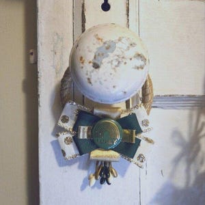 May include: A white door knob with a green and gold bow with a gold button that says "Lucky" on it.