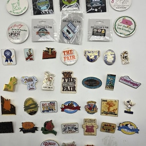 May include: A collection of assorted metal and plastic pins featuring various designs, logos, and text related to the Washington State Fair, also known as the Puyallup Fair. The pins include circular, rectangular, and custom shapes with colorful graphics.