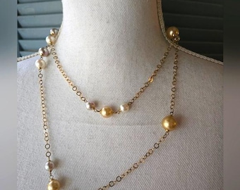 Puede incluir: Un collar de cadena dorada con perlas blancas y doradas. El collar está en capas y tiene una longitud larga.
