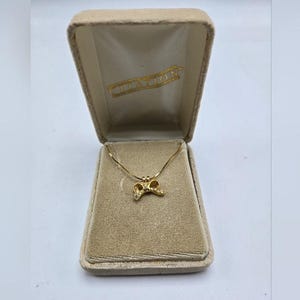 May include: A gold necklace with a small bow pendant in a velvet box. The box is labeled "Clayton".