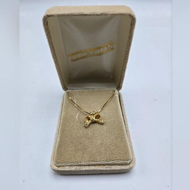 May include: A gold necklace with a small bow pendant in a velvet box. The box is labeled "Clayton".