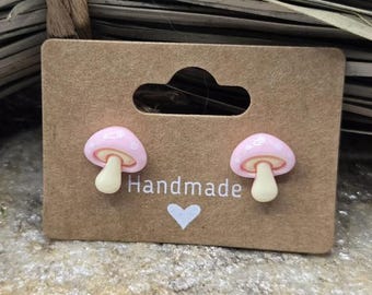 May include: A pair of pink mushroom stud earrings on a brown card with the word "Handmade" printed on it.