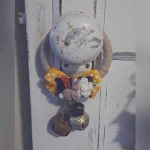 Puede incluir: Un pomo de puerta decorado con un lazo amarillo y blanco de lunares, un pequeño amuleto de conejo y tres campanas.
