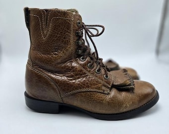 May include: Brown leather ankle boots with laces and a textured finish. The boots have a round toe, a small heel, and a decorative fringe detail on the front. The boots have the brand logo on the side.