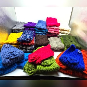 Puede incluir: Una colección de gorros y guantes de punto coloridos. Los gorros son en tonos de azul, naranja, amarillo y verde, algunos con detalles de botones. También se ven guantes rojos y verdes, junto con otros artículos de punto de varios colores.