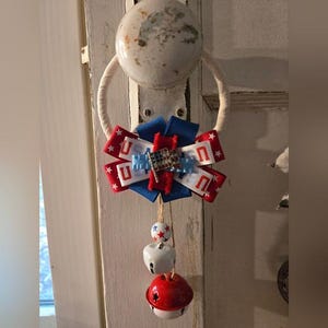 Puede incluir: Adorno patriótico para puerta con lazo rojo, blanco y azul con letras "U" y estrellas. Debajo del lazo, tres campanas: una roja, una blanca y otra con estrellas rojas.