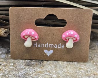 May include: A pair of pink mushroom stud earrings with white polka dots on a brown card with the word "Handmade" and a heart.