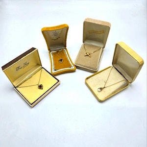 May include: Four small, yellow velvet jewelry boxes with gold necklaces inside. The boxes are on a white surface. The necklaces have different pendants, including a heart, a teardrop, and a butterfly.