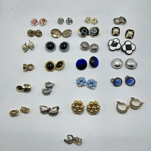 Könnte beinhalten: Eine Sammlung von 20 Paaren vintage Ohrclips in verschiedenen Stilen und Farben, darunter Schwarz, Blau, Silber, Gold und Weiß.