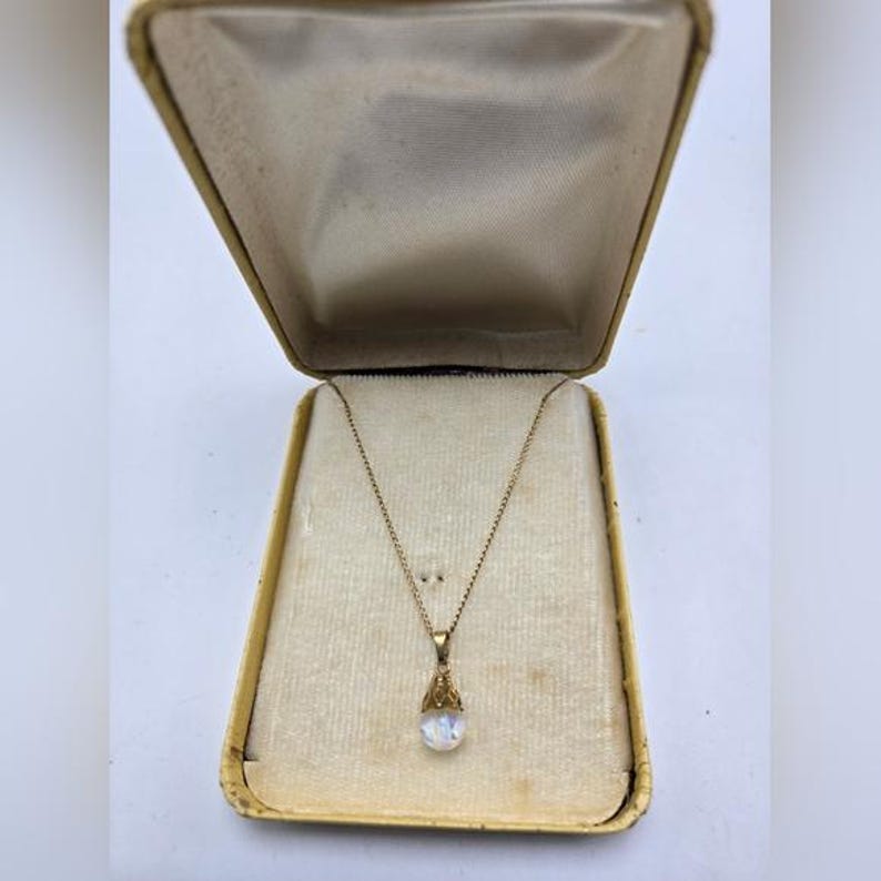 May include: A gold chain necklace with a teardrop-shaped pendant featuring a white iridescent stone.