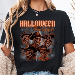 May include: Black t-shirt with a Halloween theme. The shirt features a graphic of several skulls wearing cowboy hats and bandanas, with the words "HALLOWEEN horror" in orange lettering. The design has a vintage, distressed look.