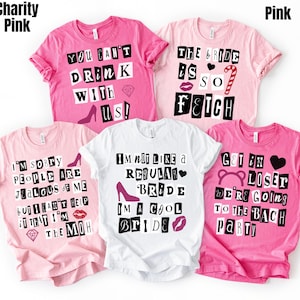 May include: A collection of pink and white t-shirts with various text designs. The shirts feature phrases like "You Can't Drink With Us!" and "The Bride is So Fetch." Some shirts have high heel and lip graphics.