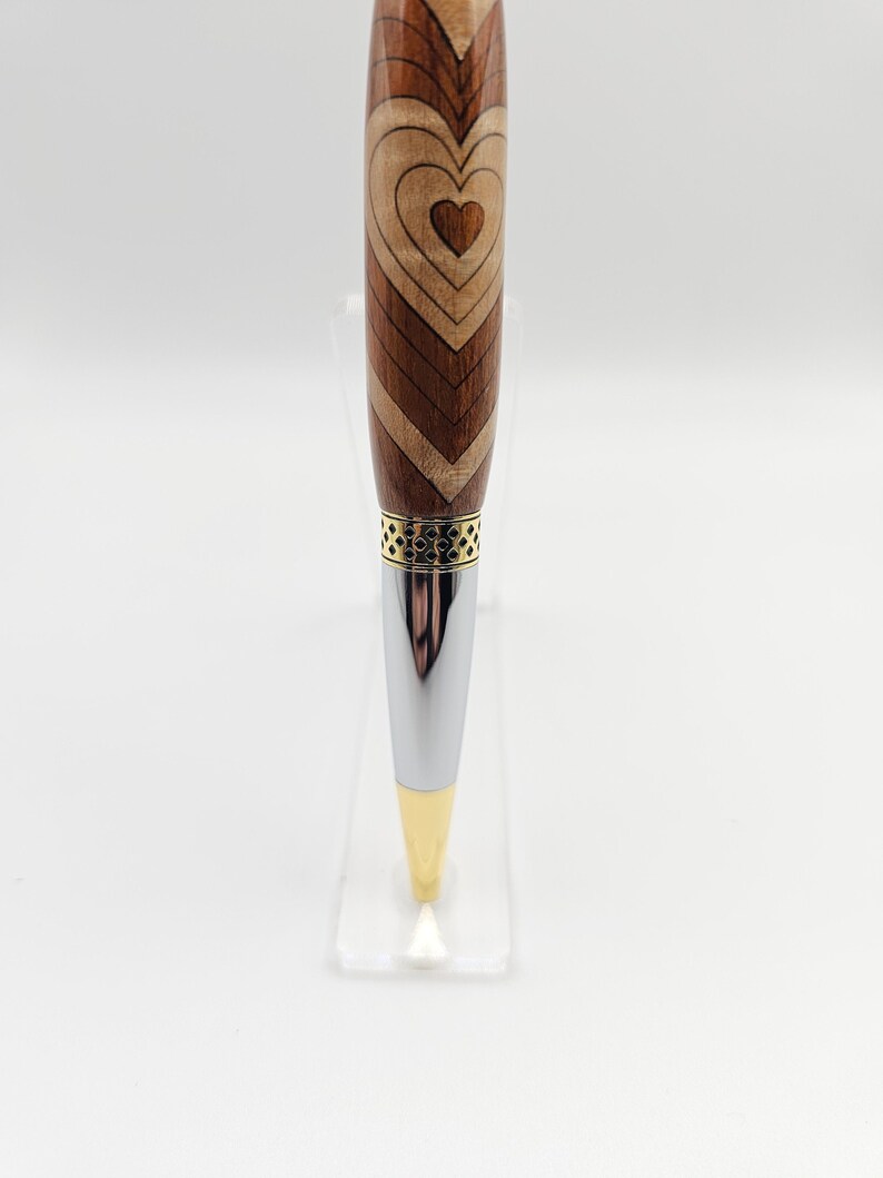 May include: A wooden pen with a heart design and a gold and silver metal trim.