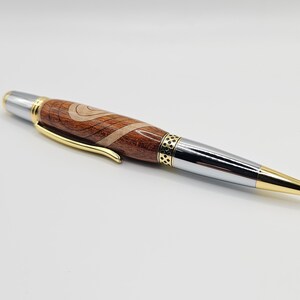 May include: A wooden and metal pen with a brown and white wood grain pattern. The pen has a gold band and a silver tip.