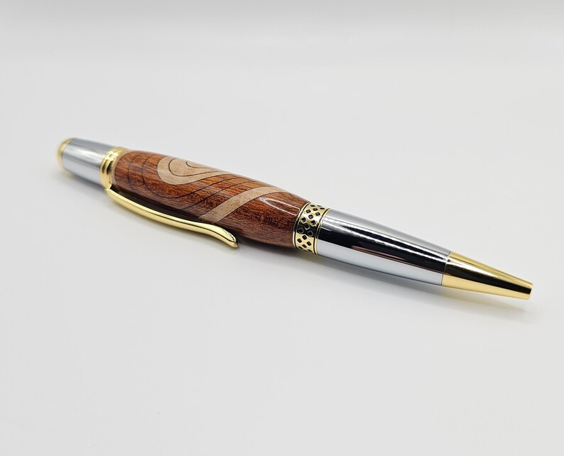 May include: A wooden and metal pen with a brown and white wood grain pattern. The pen has a gold band and a silver tip.