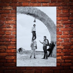 Puede incluir: Fotografía en blanco y negro de cuatro hombres de pie bajo un arco. Los hombres visten ropa de estilo occidental. El hombre en la parte superior de la pila sostiene una campana.