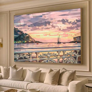 Pode incluir: Pintura de paisagem emoldurada que retrata uma cena costeira ao pôr do sol. A obra de arte apresenta um veleiro na água, uma balaustrada detalhada e um céu colorido com tons de rosa, laranja e azul. A pintura está acima de um sofá branco.