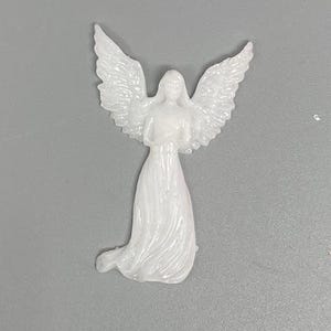 May include: A white angel figurine with outstretched wings and a flowing gown. The angel is holding its hands together in a prayerful pose. The figurine is made of a smooth, glossy material.
