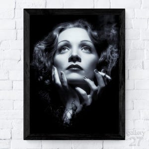 May include: A black and white framed portrait print featuring a close-up of a person with wavy hair, looking upward with hands near their face, holding a lit cigarette with visible smoke. The artwork is enclosed in a simple black frame.