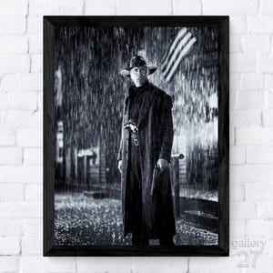 May include: Black and white framed print of a man in a long coat and hat standing in the rain, holding a gun. The American flag is visible in the background. The print is in a black frame.