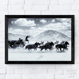 Peut inclure: Tirage encadré en noir et blanc d'une scène de poursuite en diligence. Une diligence est tirée par des chevaux, avec une personne sautant du haut. L'arrière-plan présente une chaîne de montagnes et un ciel nuageux.
