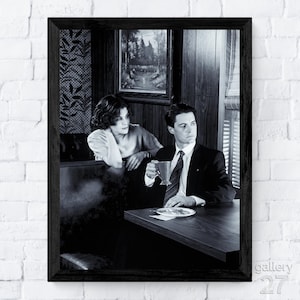 May include: Monochrome framed print depicting a man in a suit holding a mug, seated at a table with a woman in a diner setting. Includes a painting on the wall and a window with blinds.