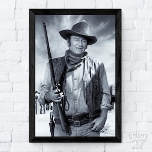 May include: Black and white framed print of a man in a cowboy hat, holding a rifle. He wears a vest, button-down shirt, and a neckerchief. The image is a portrait, with a cloudy sky in the background. The frame is black.
