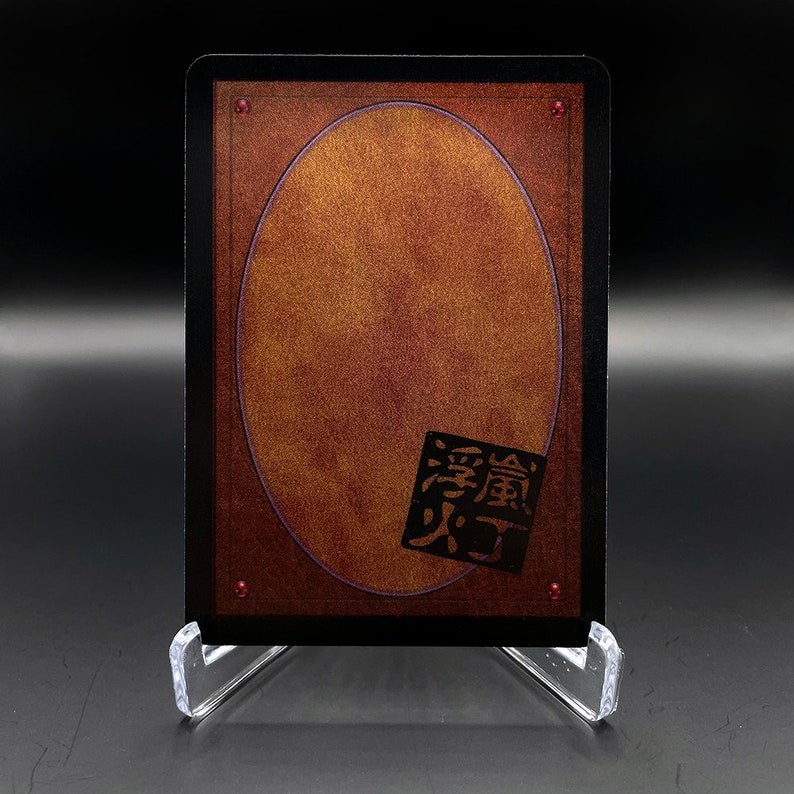 Peut inclure: Une carte noire avec une bordure rouge et un ovale dor&eacute; au centre. La carte a un symbole rouge dans le coin inf&eacute;rieur droit qui dit "火" en japonais.