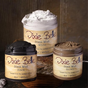 May include: Three jars of Dixie Belle Mud in white, black, and brown. Each jar has a cream-colored label with the Dixie Belle logo and product information. The white mud is piled high in its jar. The black and brown muds are visible in their respective jars.