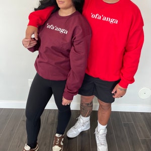 May include: Two people wearing matching sweatshirts with the text "'ofa'anga" in white lettering. The sweatshirt on the left is maroon and the sweatshirt on the right is red.