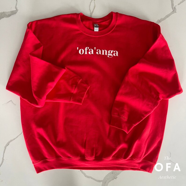 May include: Red sweatshirt with white text that says "'ofa'anga" on the front. The text is centred on the chest. The sweatshirt is a classic crew neck style.