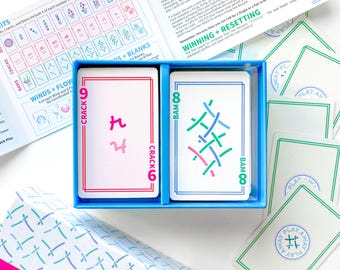 May include: Two playing cards from a game called "Play Away". The cards are blue and white with green and pink accents. The cards have the numbers 6 and 8 on them. The card on the left has the word "Crack" and the card on the right has the word "Bam".