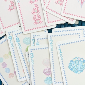 Pode incluir: Um conjunto de cartas de jogar coloridas com tema n&aacute;utico. As cartas apresentam imagens de conchas, caranguejos e as palavras "DOT" e "CRACK" com n&uacute;meros.