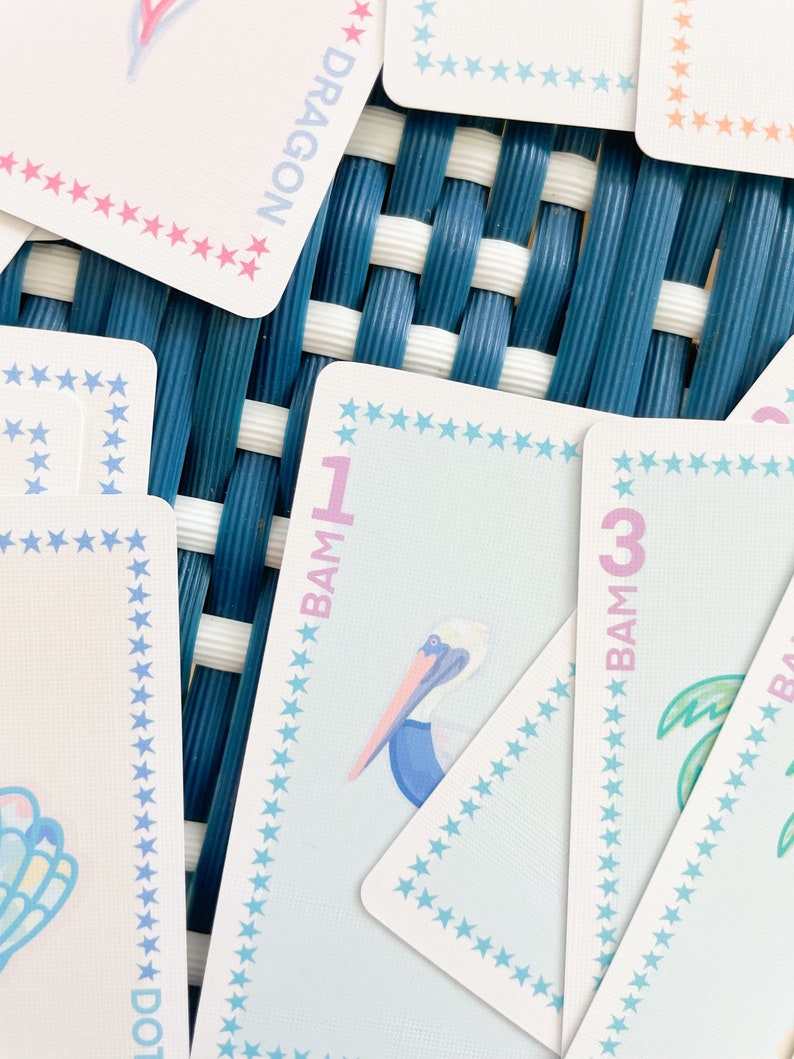 Pode incluir: Close-up de um jogo de cartas azul e rosa com uma ilustra&ccedil;&atilde;o de pelicano e o texto "BAM 1" no cart&atilde;o. O cart&atilde;o tem uma borda de estrelas azuis e rosas.