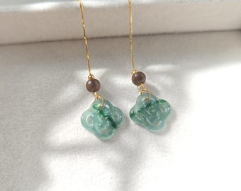 May include: A pair of green jade earrings with a gold chain and a brown wooden bead. The jade is carved into a knot design.