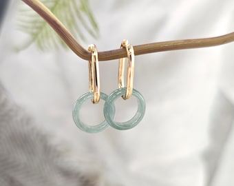 May include: A pair of gold hoop earrings with a light green jade stone accent. The earrings are hanging from a branch.