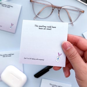 May include: Square sticky notes with the text "This meeting could have been an email" and a small graphic of an ID badge. The notes are white with a gradient of purple and blue. Other notes, glasses, and a pen are also visible.